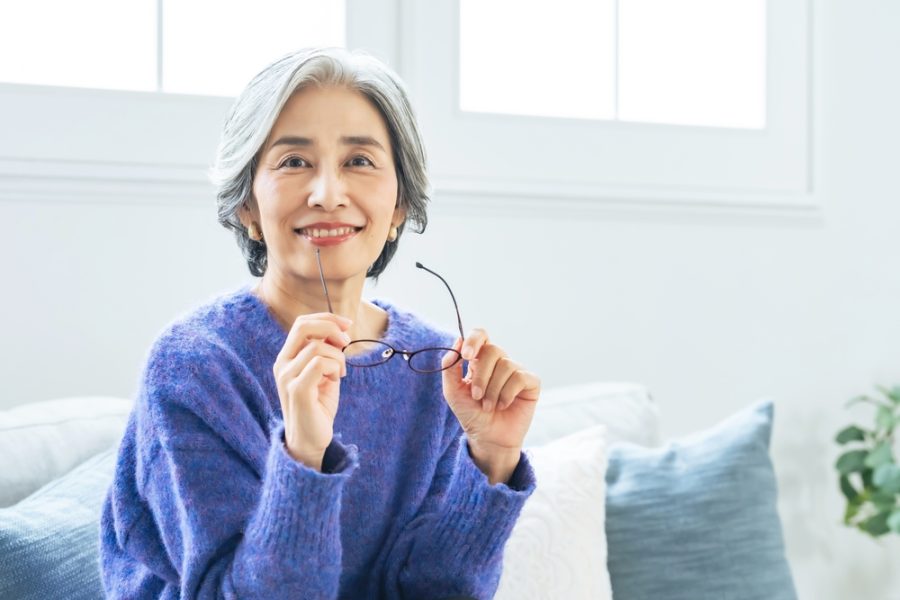 Smiling woman holding her eyeglasses indoors, representing everyday use and benefits of multifocal eyewear - whats progressive lenses