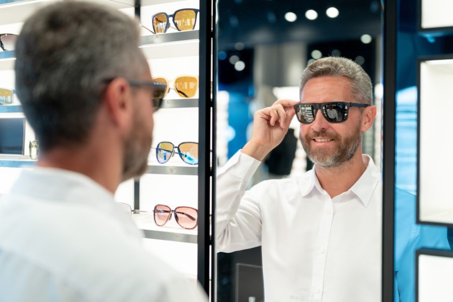 Man wearing polarized sunglasses while looking in a mirror at an eyewear store, demonstrating reduced glare and enhanced visibility benefits - polarized lenses for driving