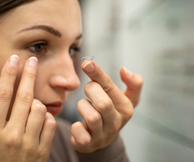 Close-up of a woman carefully touching her eye while testing contact lenses, representing a trial contact lens fitting process - how long does trial contact lenses last