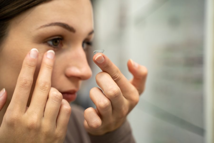 Close-up of a woman carefully touching her eye while testing contact lenses, representing a trial contact lens fitting process - how long does trial contact lenses last
