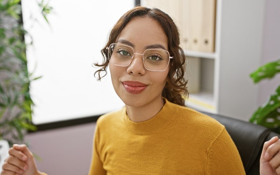 Woman wearing clear-frame eyeglasses in an office setting, representing eyewear maintenance and frame repair needs - replacement screw for glasses