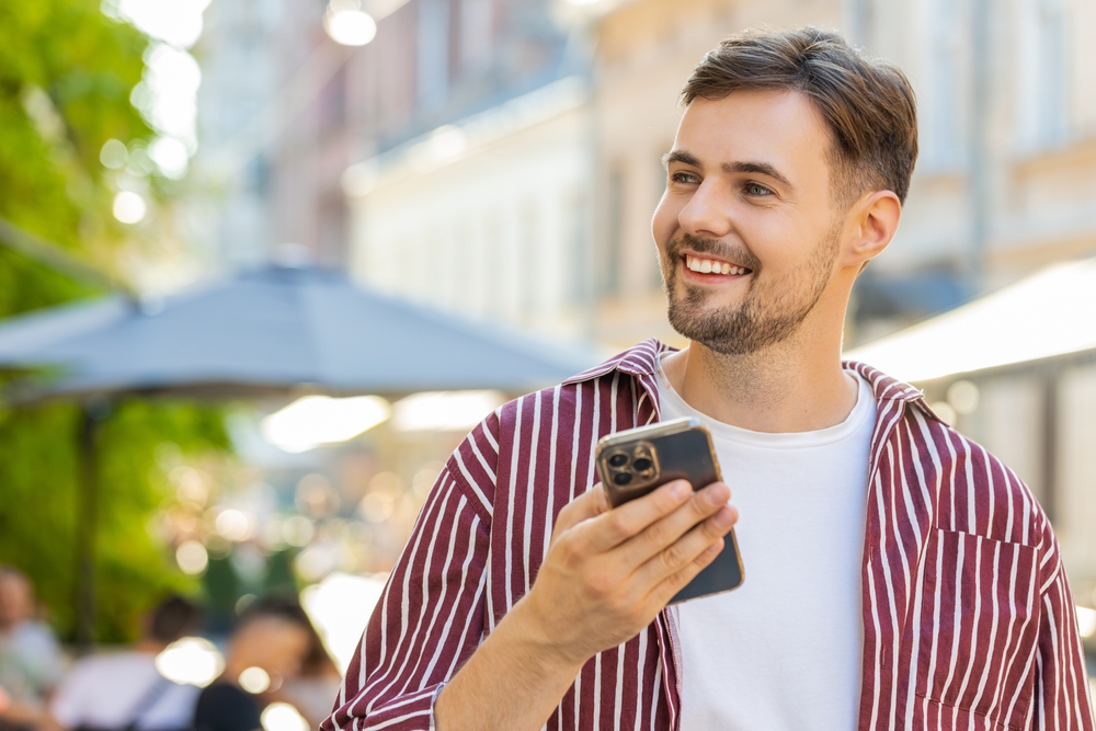 Smiling man holding a smartphone outdoors, representing convenient same-day vision care and accessibility for patients seeking services - walk in eye exam fargo nd